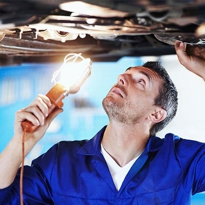 image of a mechanic holding a light looking under a car